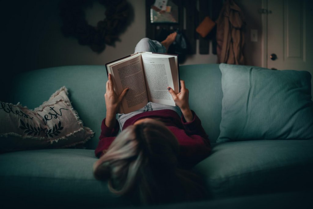 Una mujer relajándose en un sofá mientras está absorta en un libro, disfrutando de una apacible sesión de lectura